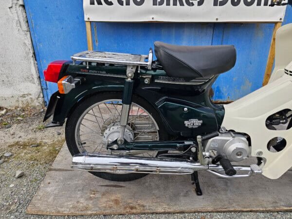 Close-up of the rear section of the 2002 Honda Super Cub C50, highlighting the rear suspension, chrome exhaust, and rear wheel.