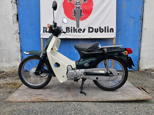 Full side view of the 2002 Honda Super Cub C50, displaying its entire body, wheels, and chrome accents.