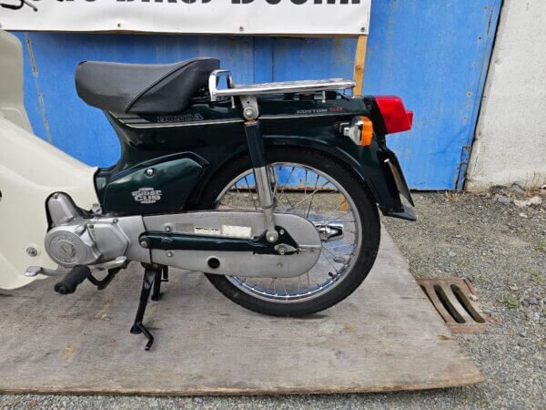 Close-up of the rear section of the Honda Super Cub C50, featuring the rear wheel, luggage rack, and "Custom 50" badging.