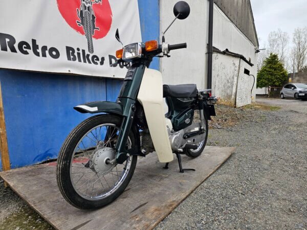Honda Super Cub C50 captured from a three-quarter front view, showcasing its round headlight, indicators, and front fender.