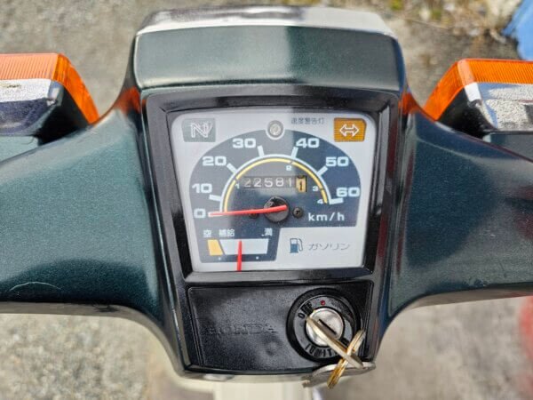 Close-up of the Honda Super Cub C50's speedometer showing 22,581 km, neutral gear indicator, and fuel gauge.