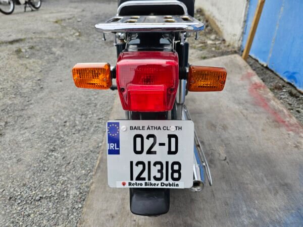 Rear view of a 2002 Honda Super Cub C50 with an Irish license plate, showcasing its tail light, indicators, and luggage rack.